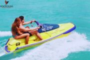 A couple riding a jet ski on calm, turquoise waters under a beautiful blue sky.