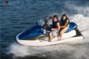 A couple enjoying a thrilling double jet ski ride on a sleek blue jet ski, splashing through calm waters.