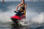 Adventurer riding a green and white jet ski with Ras Al Khaimah’s scenic shoreline in the background.