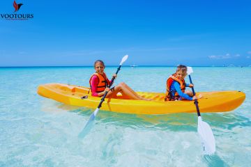 Two kids kayaking in a yellow kayak on clear turquoise water.