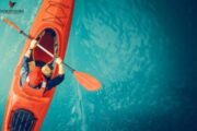 Kayaker paddling on vibrant blue water.