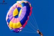 Vibrant parachute soaring against a bright blue sky during a parasailing adventure.