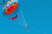 Person enjoying parasailing with a colorful parachute in a clear sky