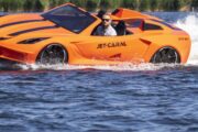 A sleek orange Jet Car speeding across calm waters, creating splashes and showcasing its futuristic design.