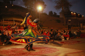 Tanoura dancer spinning in a vibrant, multicolored costume during a desert camp show