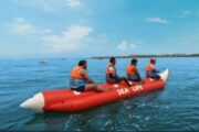 Group of four individuals enjoying a thrilling banana boat ride on the sea, wearing life jackets.