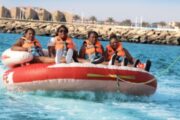 Four women seated on a red and white inflatable water tube being pulled across the water.