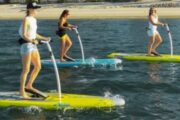 Three women enjoying an electric stand-up paddle board ride on calm waters