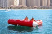 Two women seated on a Fly Fish inflatable with a cityscape in the background.