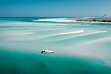 Scenic view of turquoise waters with a small boat and a pristine sandy coastline under a clear blue sky.