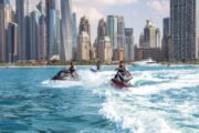 Three jet skis speeding on the waters with Dubai's skyscrapers in the background.