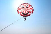 Smiling parasailing parachute in red and white design floating in the clear blue sky.