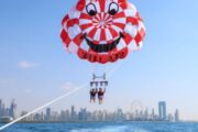 Two people parasailing high above Dubai with a red and white parachute