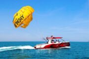 Red parasailing boat towing a birthday-themed parachute on a clear blue sea