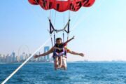 Two individuals enjoying parasailing with a vibrant red parachute over Dubai waters