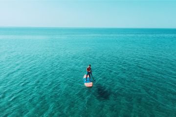 Person stand-up paddleboarding on calm turquoise waters in Dubai.