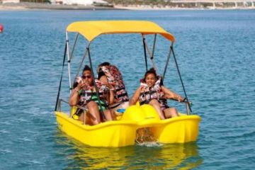 Three women enjoying a pedalo boat ride on calm blue waters in Dubai, wearing life jackets.