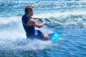 Man kneeboarding on a lake, gliding over the waves with a bright blue kneeboard.