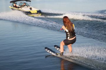 Woman water skiing behind a speedboat on a calm lake.