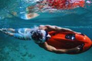 Man diving through coral reefs with a red Seabob