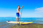 Man paddleboarding in shallow water under a clear blue sky