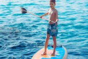 Child enjoying stand-up paddleboarding in calm blue waters.