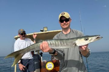 Man holding a large barracuda on a fishing boat with calm ocean waters in the background