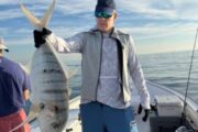 Angler holding a large striped fish on a boat with calm ocean waters in the background