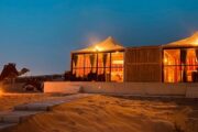 Illuminated desert chalets with camel and bonfire at night.