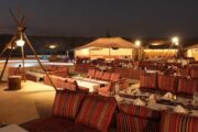 A traditional Arabian majlis dining area with red cushions and low tables under the night sky.