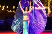 A belly dancer in a blue costume performing with large shimmering wings.