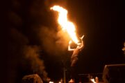 A fire performer breathing flames into the night sky at a desert camp.