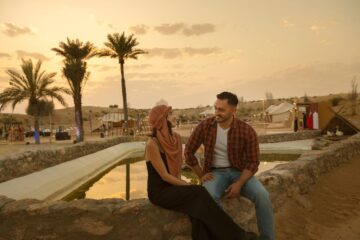 Couple at Desert Sunset | Desert Camp | Palm Trees | Sunset | Couple | Conversation | Water Pool | Sunset Hues | Romantic Atmosphere