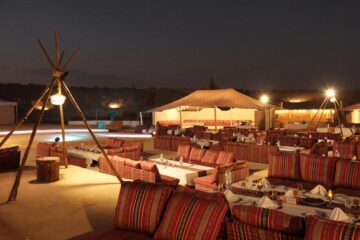 A serene desert campsite at dusk, featuring a cozy setup with a canopy tent adorned with string lights.