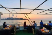 Guests dining on a yacht with the Ain Dubai Ferris wheel in the background at sunset