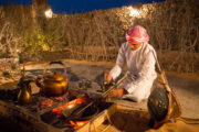 Emirati man preparing Arabic coffee by a campfire.