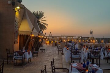 An open-air dining setup in a desert fortress at sunset with elegantly arranged tables.