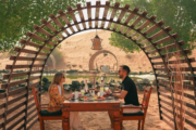 A couple dining under a wooden archway in a desert oasis.