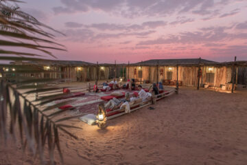 Guests relaxing in a traditional desert lounge under a vibrant sunset.