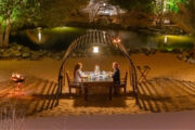 Couple dining by a serene pond under a lit arch in the desert.