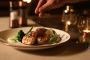 Gourmet dinner plate being meticulously garnished in a candlelit setting