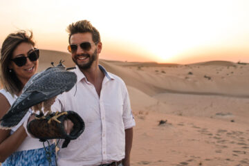 Couple holding a falcon in a desert during sunrise