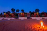 Desert camp with firepit and private tents at night.