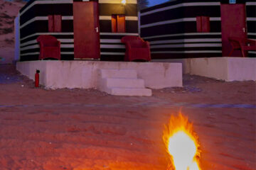 Close-up of desert campsite firepit with private tents in the background.