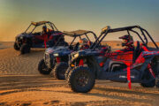 Three dune buggies on a desert slope during sunset.