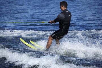 Man enjoying water skiing with bright yellow skis on a blue lake.