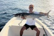 Fisherman displaying a large kingfish catch on a boat with the sea in the background.