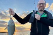 Smiling fisherman holding a grouper caught during a fishing trip.