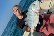 Angler displaying a silver trevally on a boat surrounded by clear blue waters