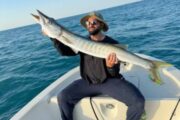 Fisherman holding a barracuda, showcasing the catch on a sunny day.